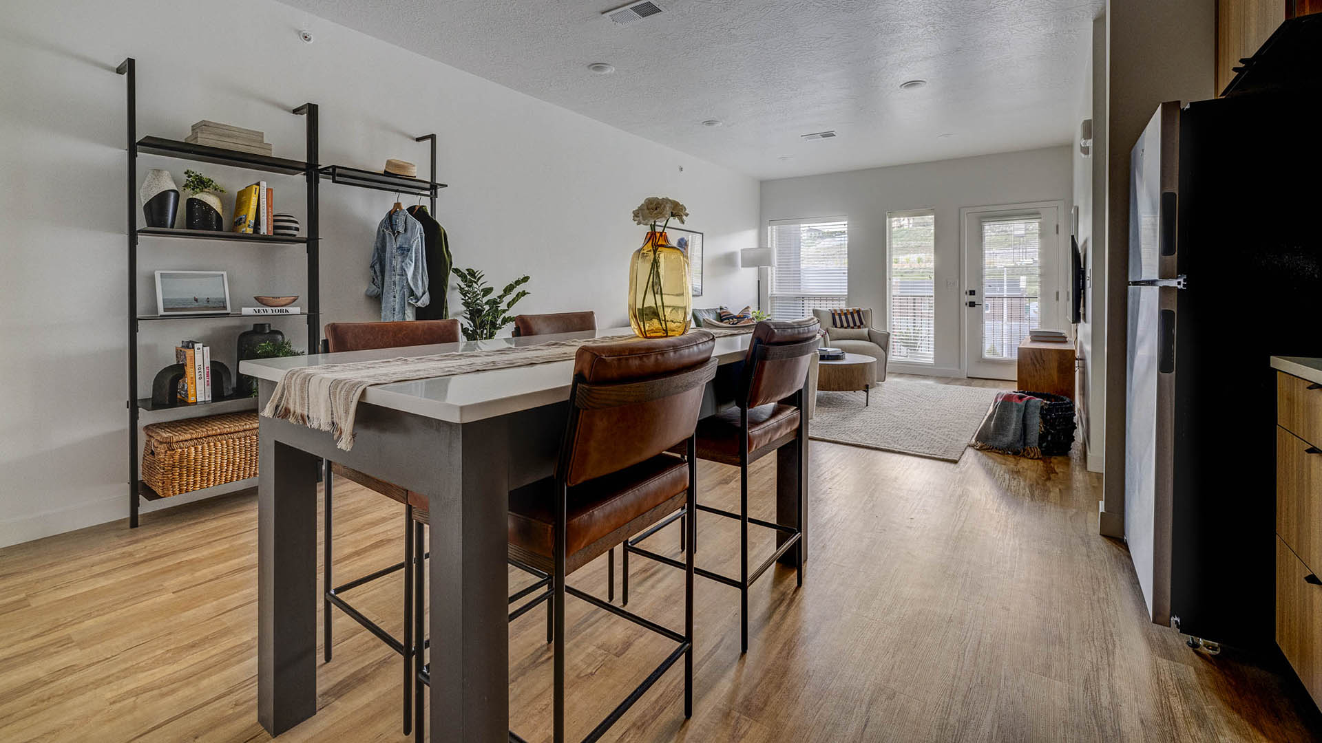Apartment living area with wood style floor, tall dining table, shelves with decor, and balcony door.